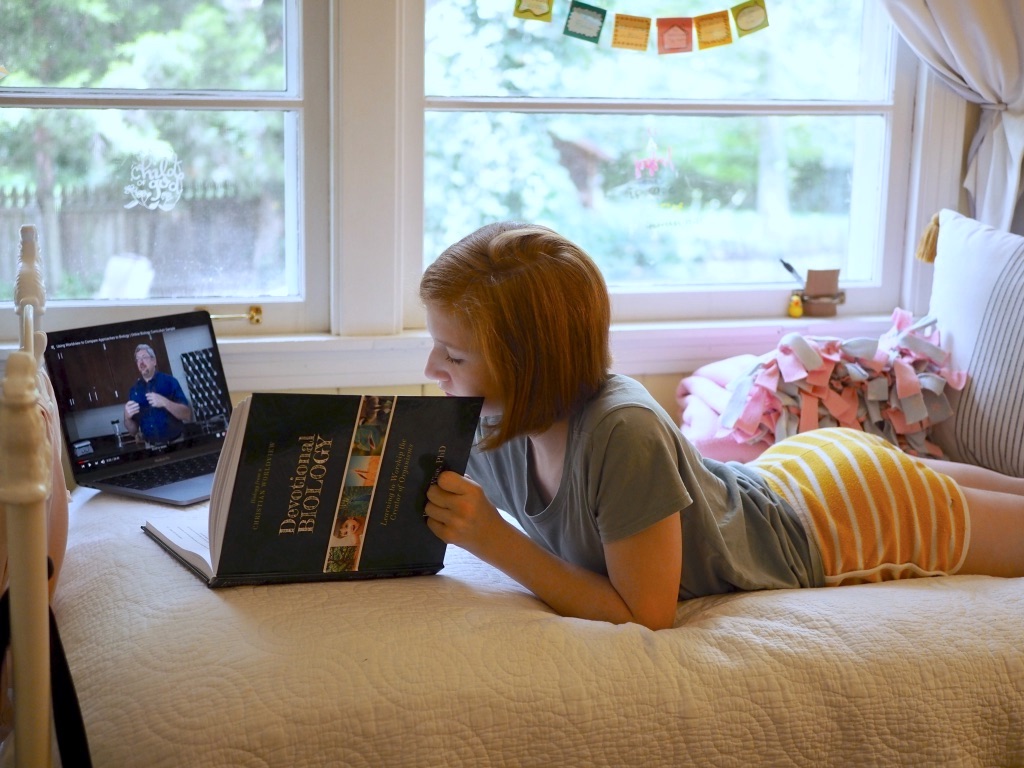 A homeschool student reading a book and following a lesson on her laptop