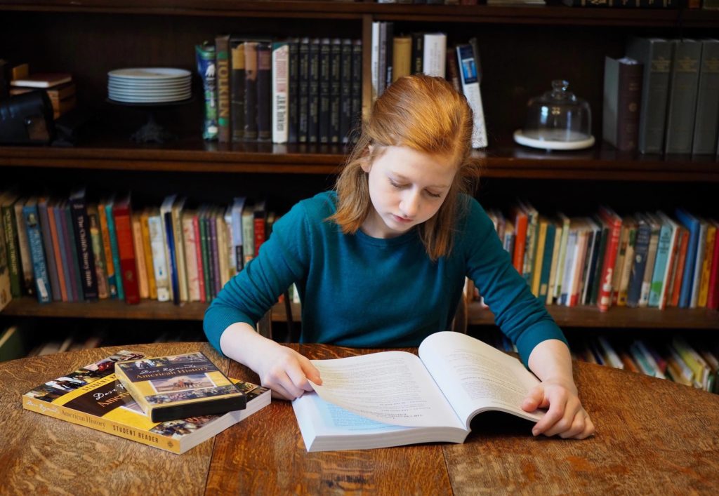 A homeschool student reading at a table in front of a bookshelf