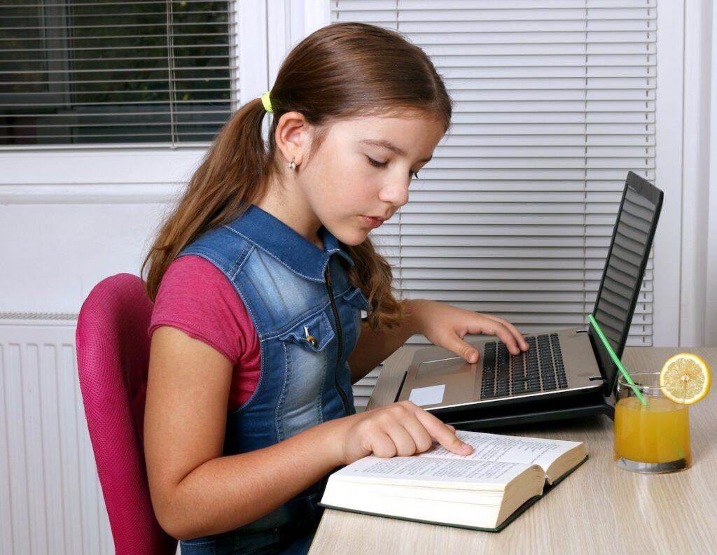 A girl studying with an open book and a laptop at her desk